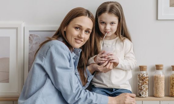 A loving mother with her daughter drinking a smoothie and sharing a warm moment in the kitchen.