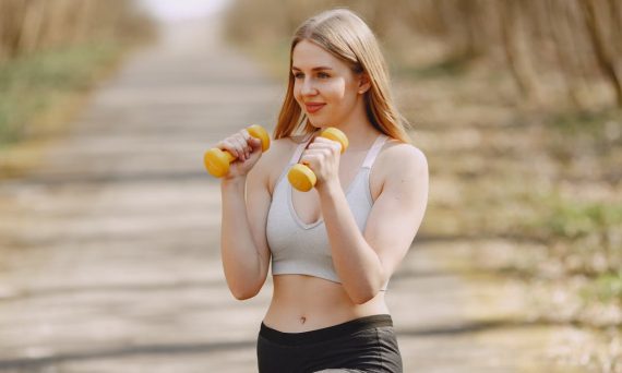 Fit woman lifting dumbbells on a sunny day, embracing a healthy outdoor workout.